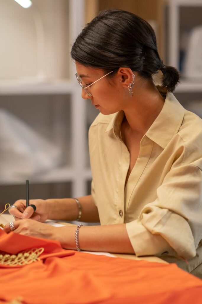 Asian female fashion designer sketching in a creative studio, focusing on textile design.