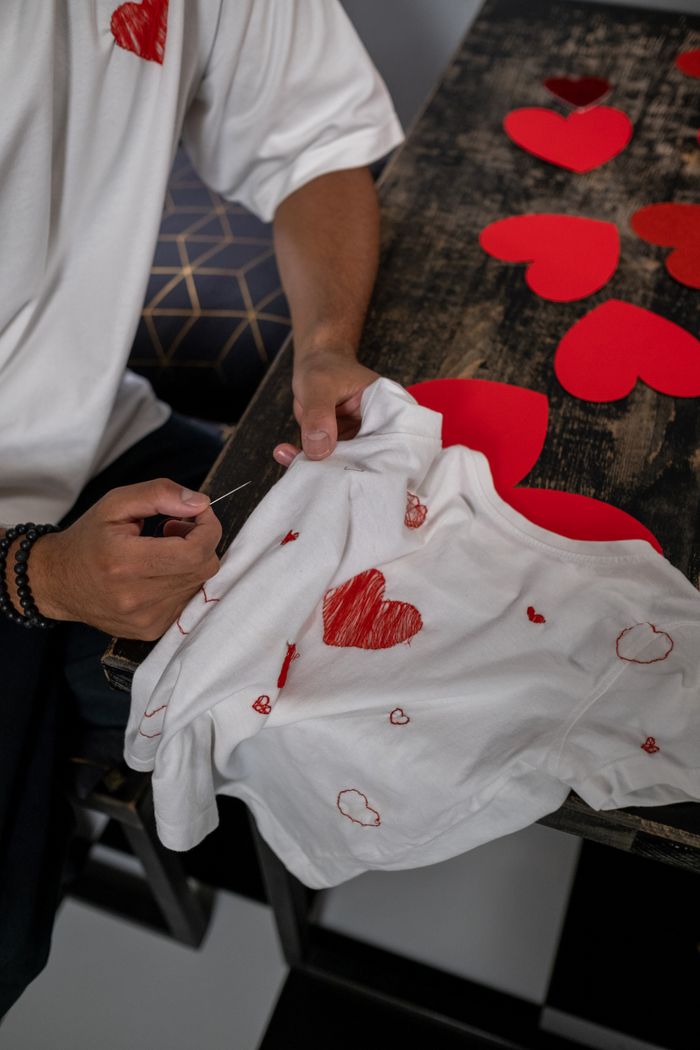 journey Person embroidering heart shapes on a white shirt, themed for Valentine's Day indoors.